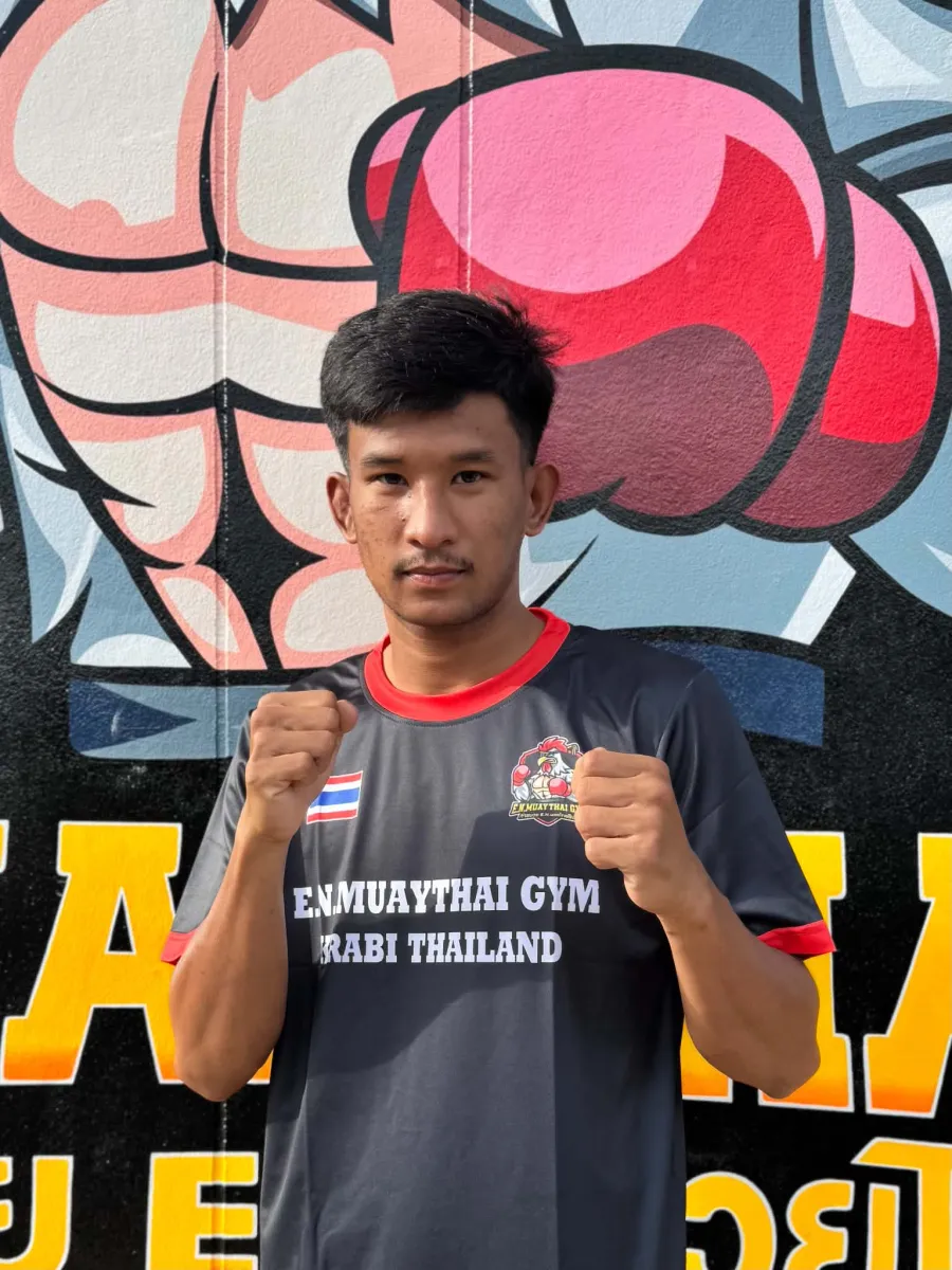 Dummylek, coach and active fighter at E.N. Muaythai Gym, in front of the gym mural in Ao Nang