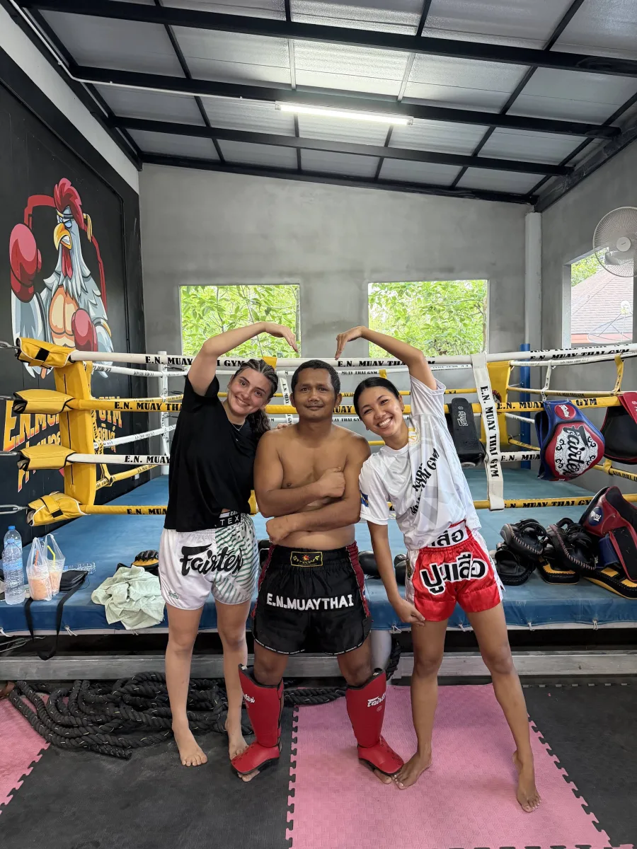 Three E.N. Muaythai Gym members smiling together in the ring