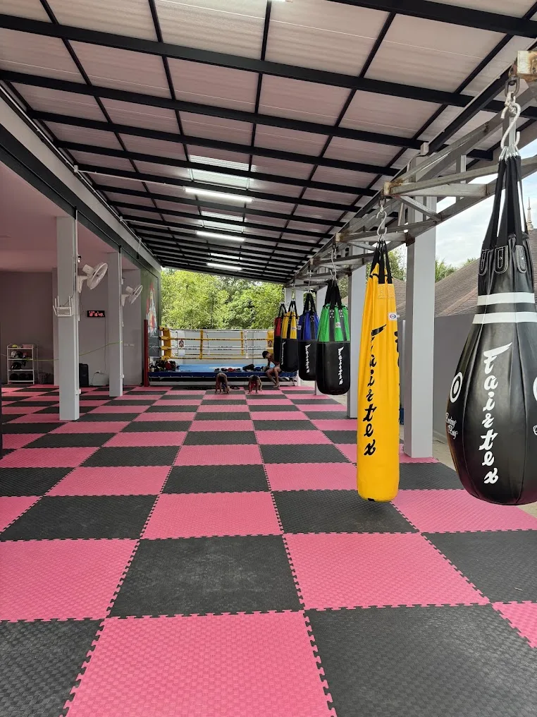 Open-air training floor with pink and black mats, hanging Fairtex bags and the ring at the far end of E.N. Muaythai Gym in Ao Nang